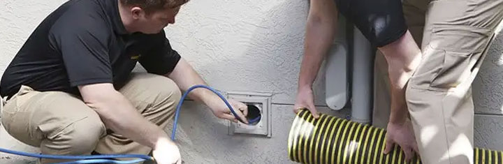 Two Stanley Steemer technicians work together to clean a customer's dryer vent using special equipment