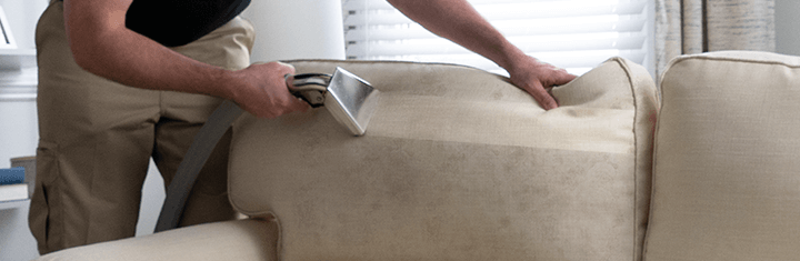 Stanley Steemer technician pulling vacuum attachment along couch to remove dirt and dust