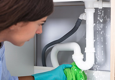 Woman inspecting a leaking pipe under a sink. 